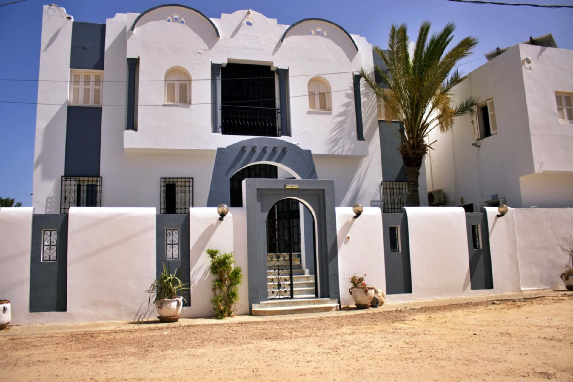 Façade blanche et bleue de la Résidence Les Palmiers à Djerba avec palmiers